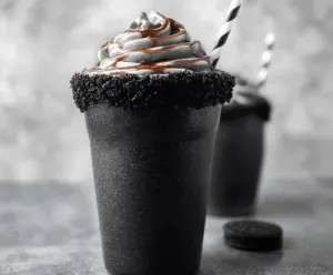 Creamy black milkshake topped with whipped cream and chocolate sprinkles in a tall glass, perfect for a rich and indulgent dessert treat.