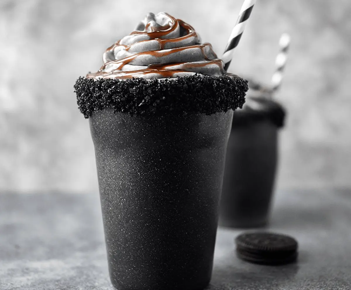 Creamy black milkshake topped with whipped cream and chocolate sprinkles in a tall glass, perfect for a rich and indulgent dessert treat.