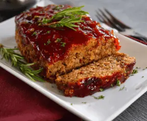 Juicy meatloaf glazed with brown sugar and ketchup topped with fresh herbs, ready to serve
