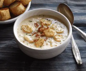 Creamy New England Clam Chowder served in a bowl with fresh herbs and oyster crackers, showcasing a comforting seafood soup.
