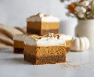 Delicious pumpkin blondie cheesecake bars with a creamy topping and fall-inspired flavors on a rustic wooden table