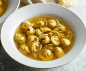 A bowl of delicious tortellini en brodo featuring tender pasta filled with cheese and meat, served in a flavorful clear broth garnished with fresh herbs.