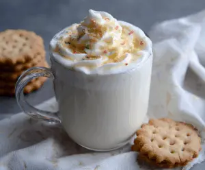 Creamy sugar cookie white hot chocolate topped with whipped cream and sprinkles, perfect for winter holidays.