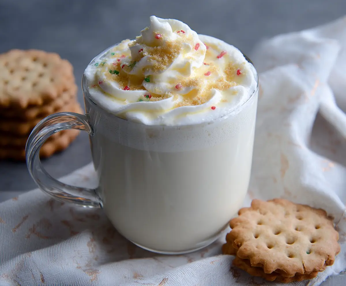 Creamy sugar cookie white hot chocolate topped with whipped cream and sprinkles, perfect for winter holidays.