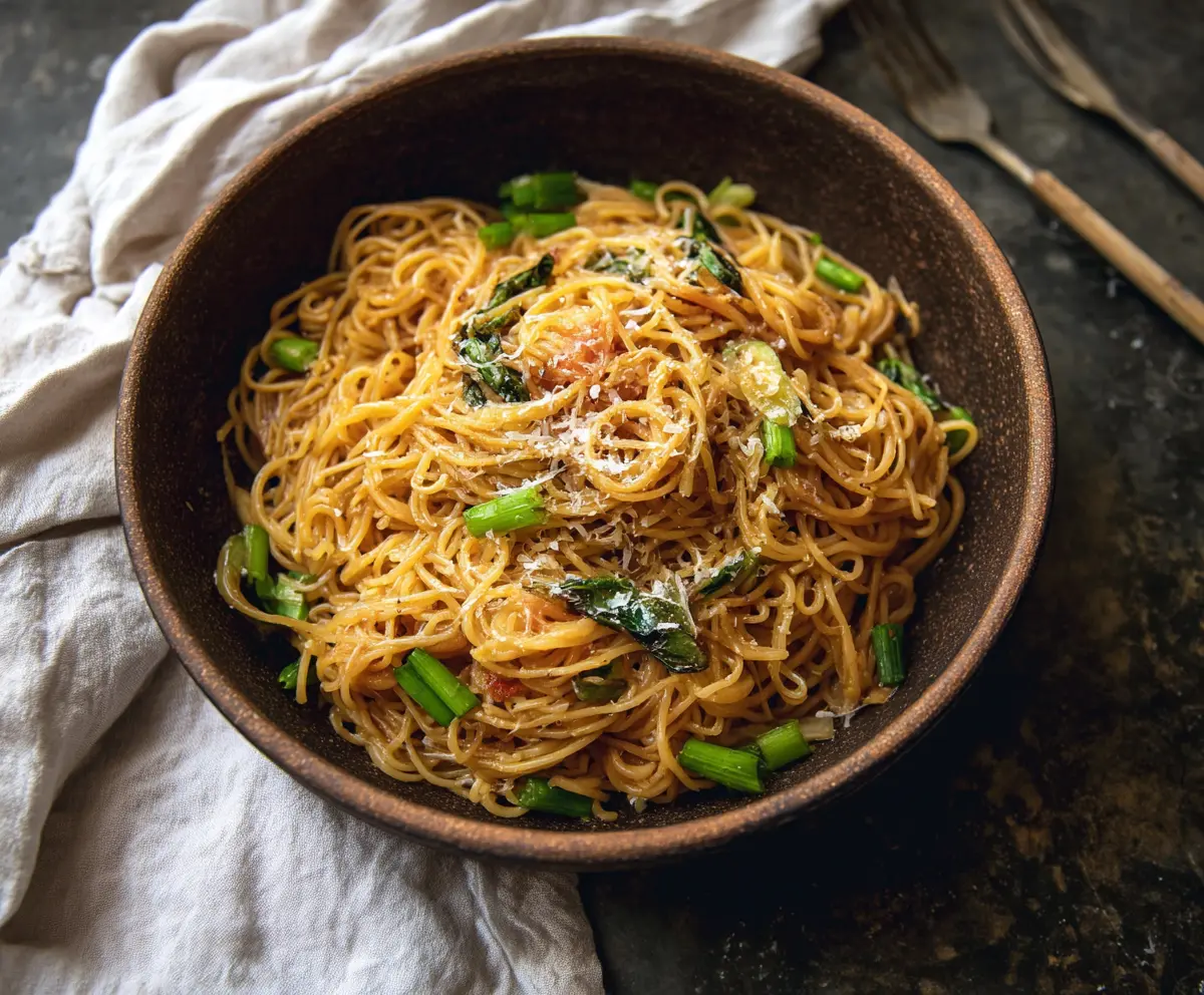 Delicious Asian garlic noodles garnished with green onions on a white plate.