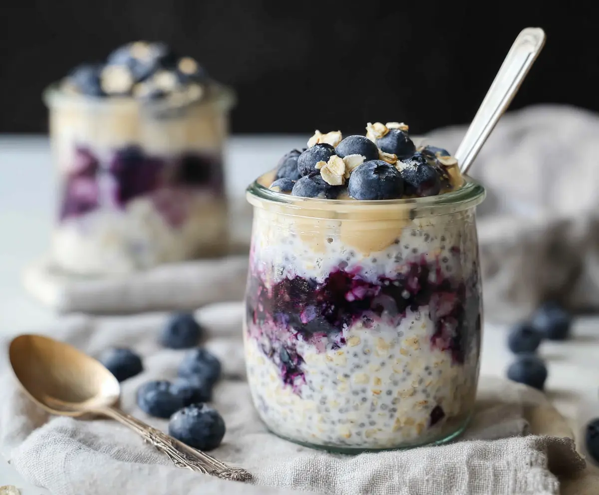 Creamy blueberry cheesecake overnight oats topped with fresh blueberries and a sprig of mint.