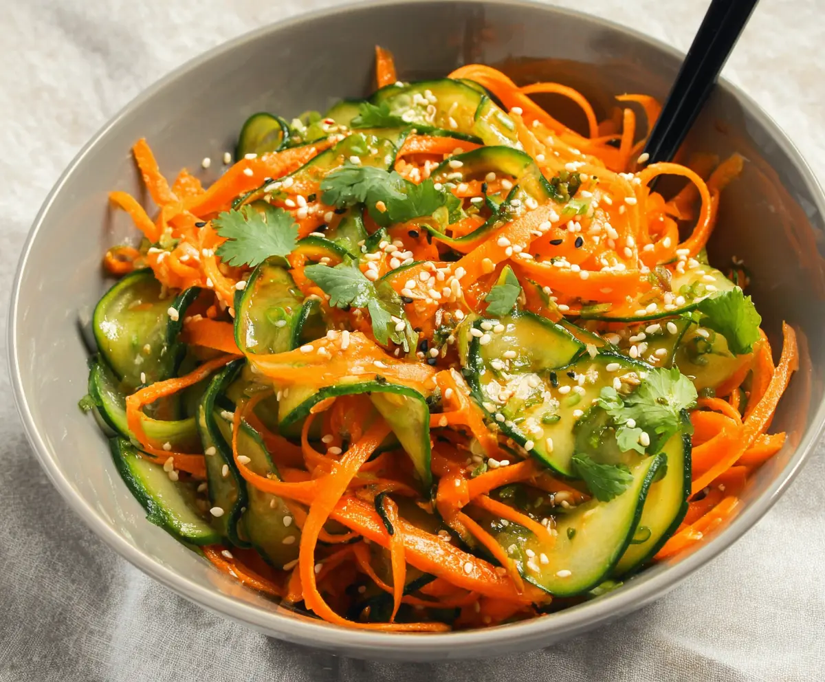 Colorful Asian carrot and cucumber salad in a bowl, garnished with sesame seeds for a fresh, healthy meal.