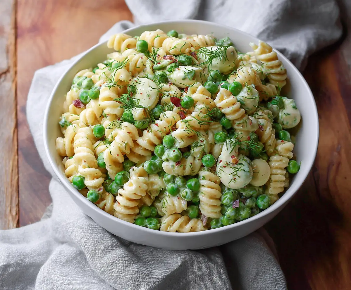 Creamy English Pea Pasta Salad with fresh herbs and colorful vegetables on a white plate.