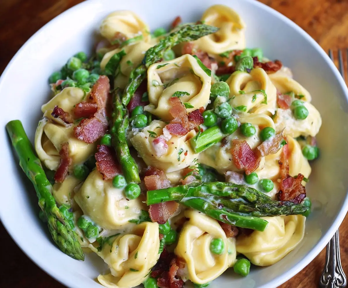 Delicious tortellini pasta with peas, asparagus, and crispy bacon on a white plate.