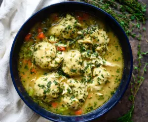 A bowl of spring chicken and dumpling soup garnished with fresh herbs, showcasing a comforting homemade meal.