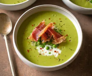 Savory spring pea soup topped with crispy prosciutto slices on a rustic plate.
